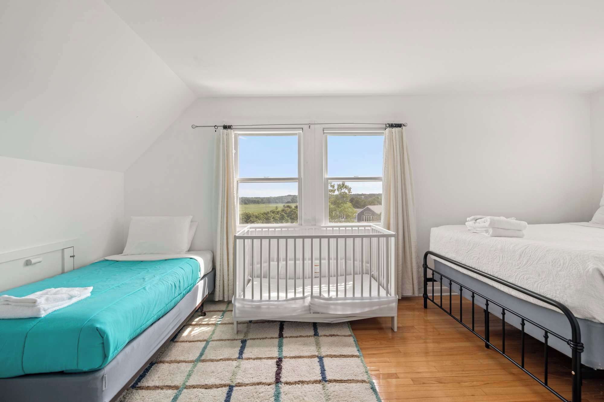 A bedroom with two beds, a crib, and a large window with a view of the countryside.