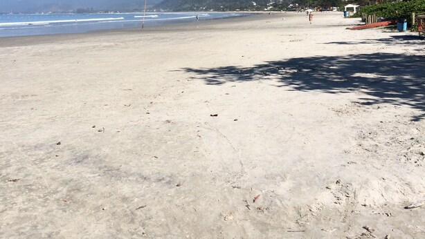 A wide sandy beach with a clear sky and mountains in the background. - Comfortable house (large balcony and garden), 70 meters from the beach with Wi-Fi.   (praia da lagoinha ubatuba)