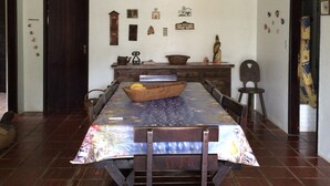 A dining area with a large table, chairs, a hanging green light fixture, and a wall with various decorative items. - Comfortable house (large balcony and garden), 70 meters from the beach with Wi-Fi.   (praia da lagoinha ubatuba)