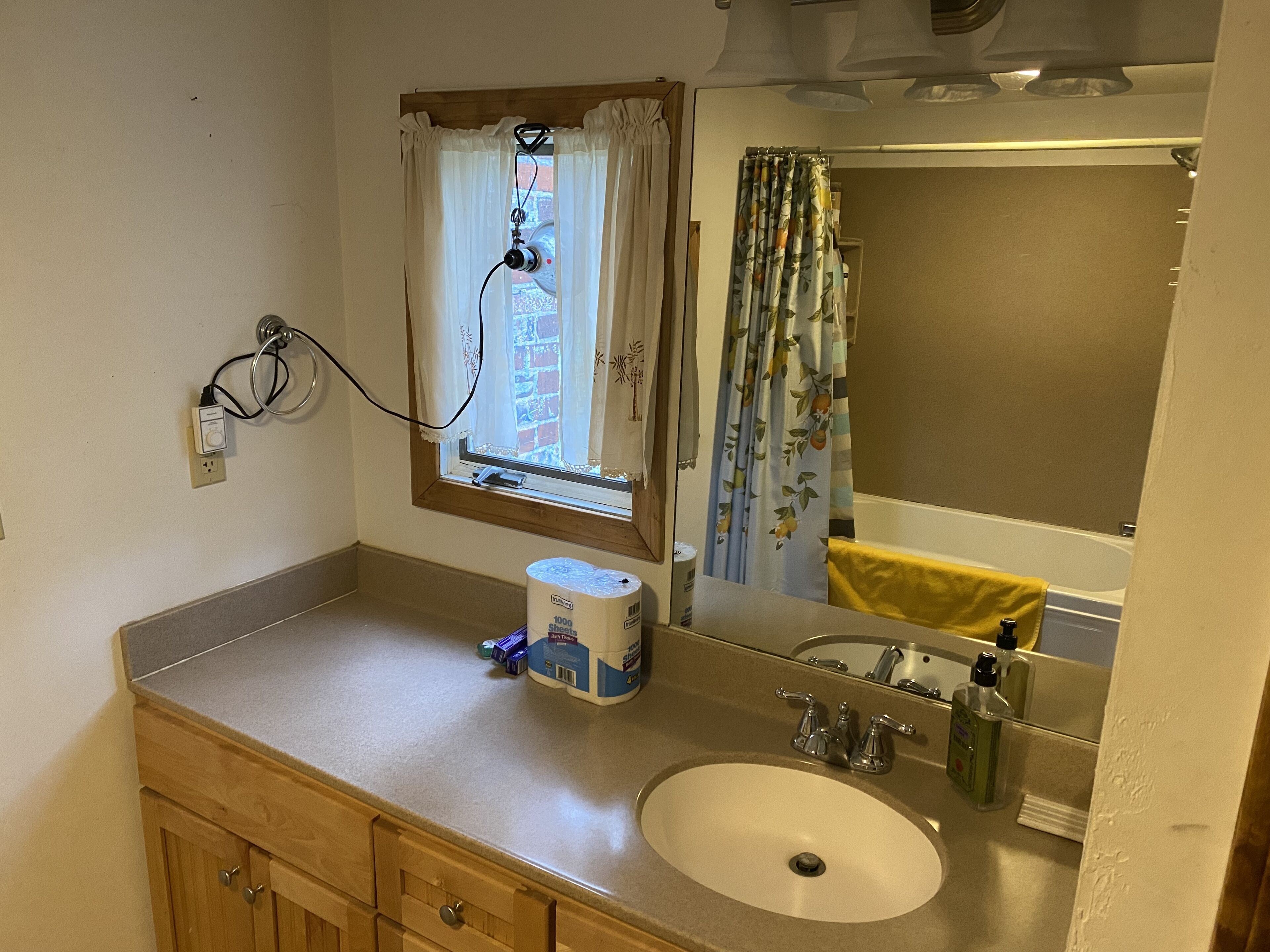 A bathroom with a sink, mirror, window with curtains, and a towel hanging on the wall.