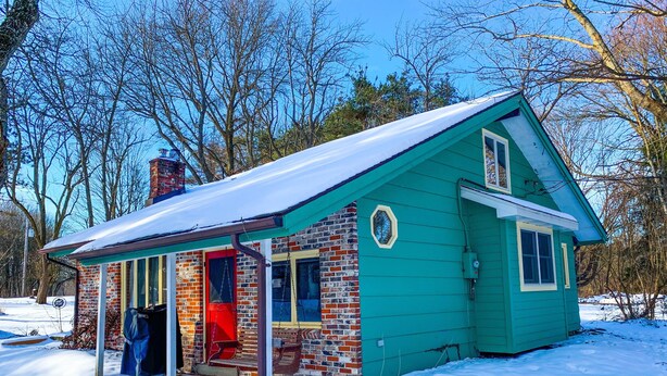 Une petite maison à deux étages, à l’extérieur vert et à la porte rouge, entour ée de neige.