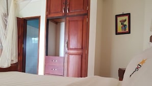A bedroom with a bed, a wooden wardrobe, a small table, and a wall-mounted picture.