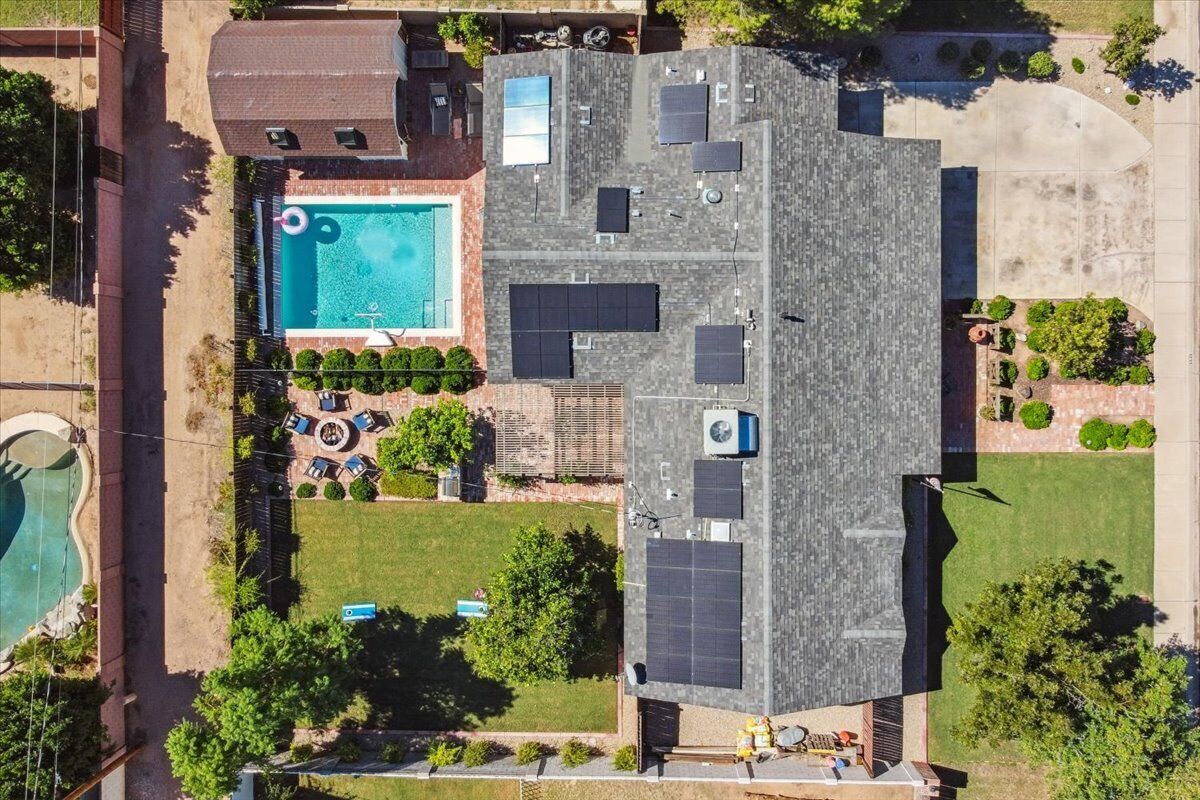 An aerial view of a residential property with a swimming pool, solar panels, and a well-maintained lawn.
