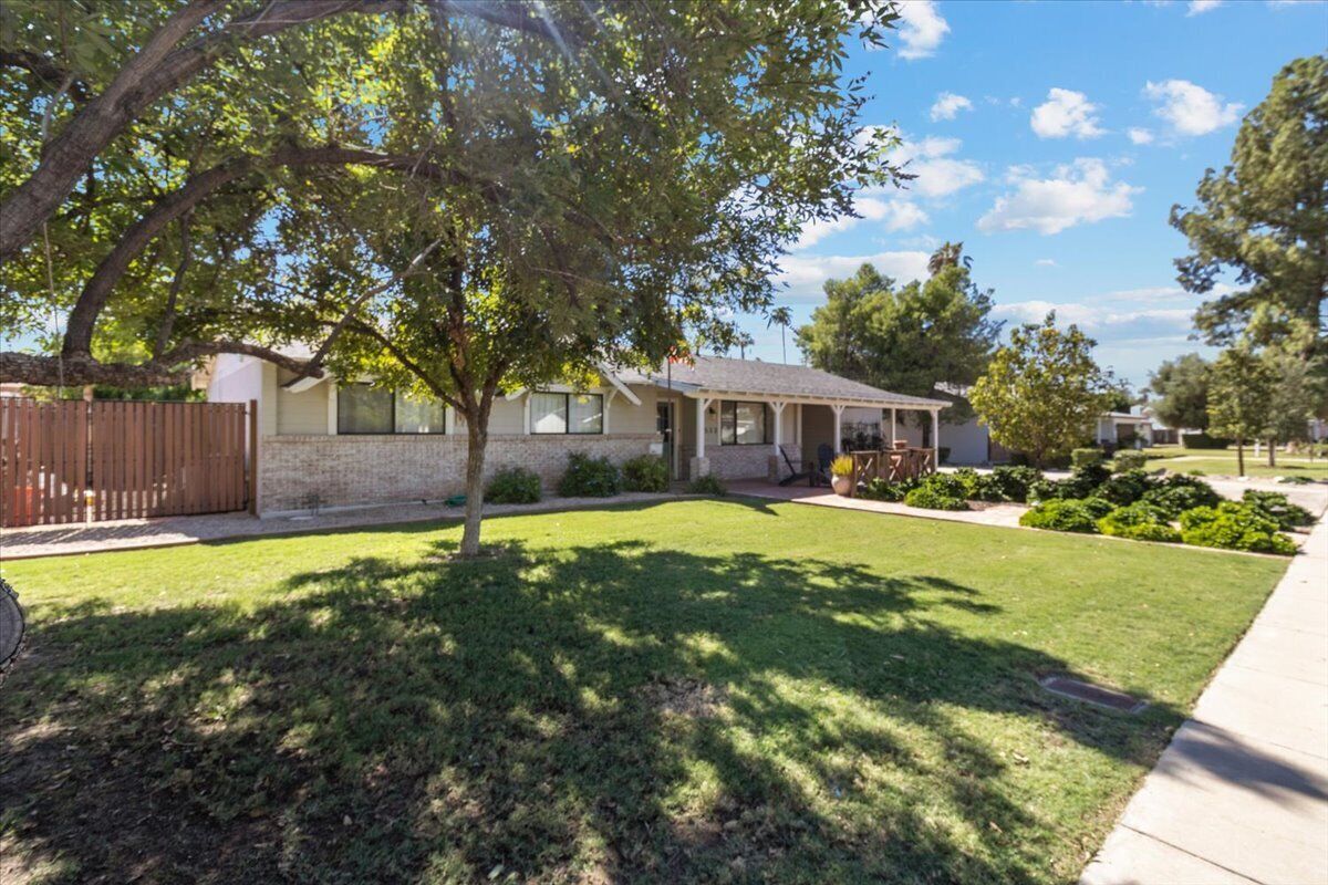 A residential house with a well-maintained lawn, a wooden fence, and a large tree providing shade.