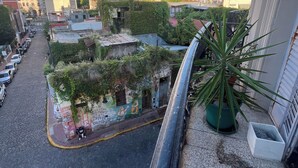 Un immeuble de grande hauteur offrant une vue sur une rue en contrebas, où l’on aperçoit des voitures garées et un petit espace jardin.