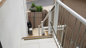 Ein Wohnbalkon mit Fliesenboden, Metallgeländer und Blick auf eine Straße mit Häusern und einem parkenden Auto.
