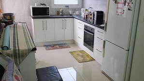 Eine kompakte Küche mit weißen Schränken, einer Mikrowelle, einem Kühlschrank und einem Fenster mit Blick auf ein Gebäude.