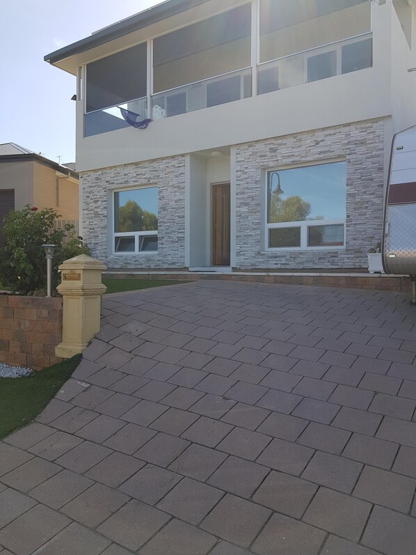 A modern two-story house with a stone facade, large windows, and a paved driveway.