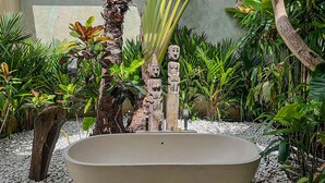 Een groot bad in een tuinsetting, met tropische planten en stenen sculpturen.