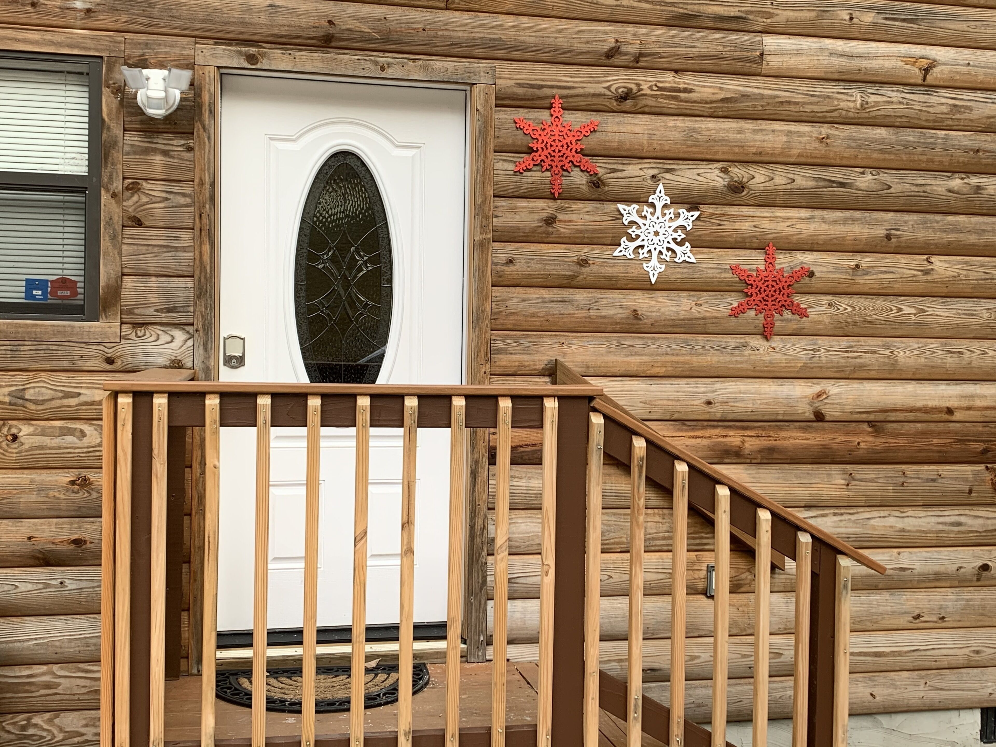 A wooden cabin with a white door, a small porch with a wooden railing, and decorative snowflakes on the wall.