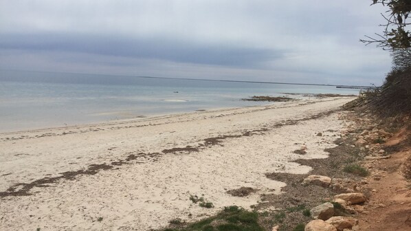 A beach with a rocky shoreline and a bridge in the distance.