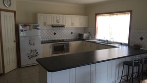 A kitchen with white cabinets, a black countertop, a microwave, a refrigerator, and a window with curtains. - Lane-way Holiday Rental -3 Minutes walk from the beach (Moonta Bay)