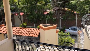 A balcony with a tiled roof, a metal railing, and a view of a parked car and trees. - HERMOSA CASA EN AJIJIC (San Antonio Tlayacapan)