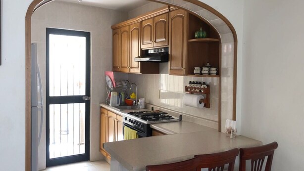 A kitchen with wooden cabinets, a stove, and a dining area with chairs. - HERMOSA CASA EN AJIJIC (San Antonio Tlayacapan)
