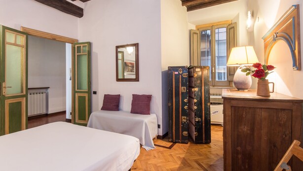 A room with two beds, wooden floors, a mirror, a lamp, and vintage suitcases. - Piazza Navona Charming Apartment (Roma)