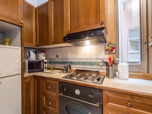 Cucina con mobili in legno, piano cottura a gas, microonde e frigorifero.