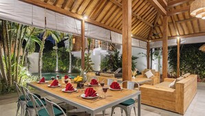 Ein Essbereich im Freien mit Pool, Holzmöbeln und tropischen Pflanzen.