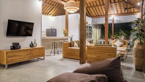 Ein modernes Wohnzimmer mit Fernseher, Holzmöbeln und einer Küche im Hintergrund.