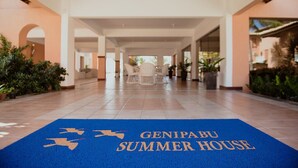 Un paseo techado con un tapete azul que dice "GENIPABU SUMMER HOUSE" conduce a un área de descanso.