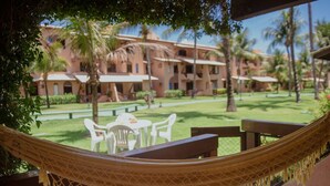 Una hamaca en un balcón con vistas a un resort, con mesas al aire libre y palmeras.