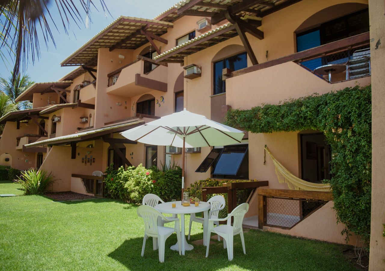Un patio con mesa y sillas, una hamaca y un edificio con balcones y una pantalla de televisión.