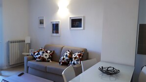 A modern living room with a beige sofa, a white coffee table, and a small table with a glass bowl. There are three framed pictures on the wall.
