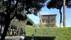 A residential building with a balcony, surrounded by trees and a hedge.