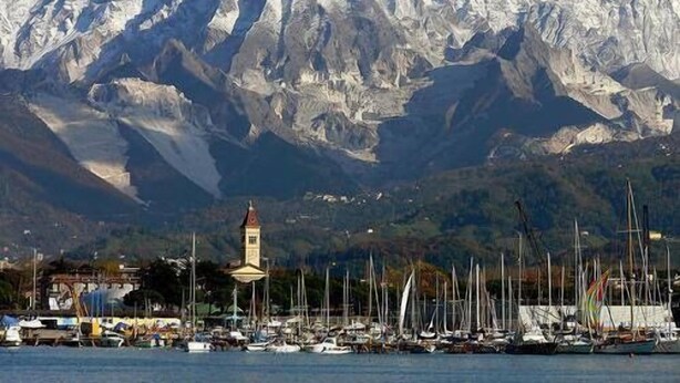 A marina with boats and a clock tower against a backdrop of snow-capped mountains.