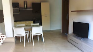 A modern living room with a sofa, a TV on a stand, and a dining area with chairs and a table.