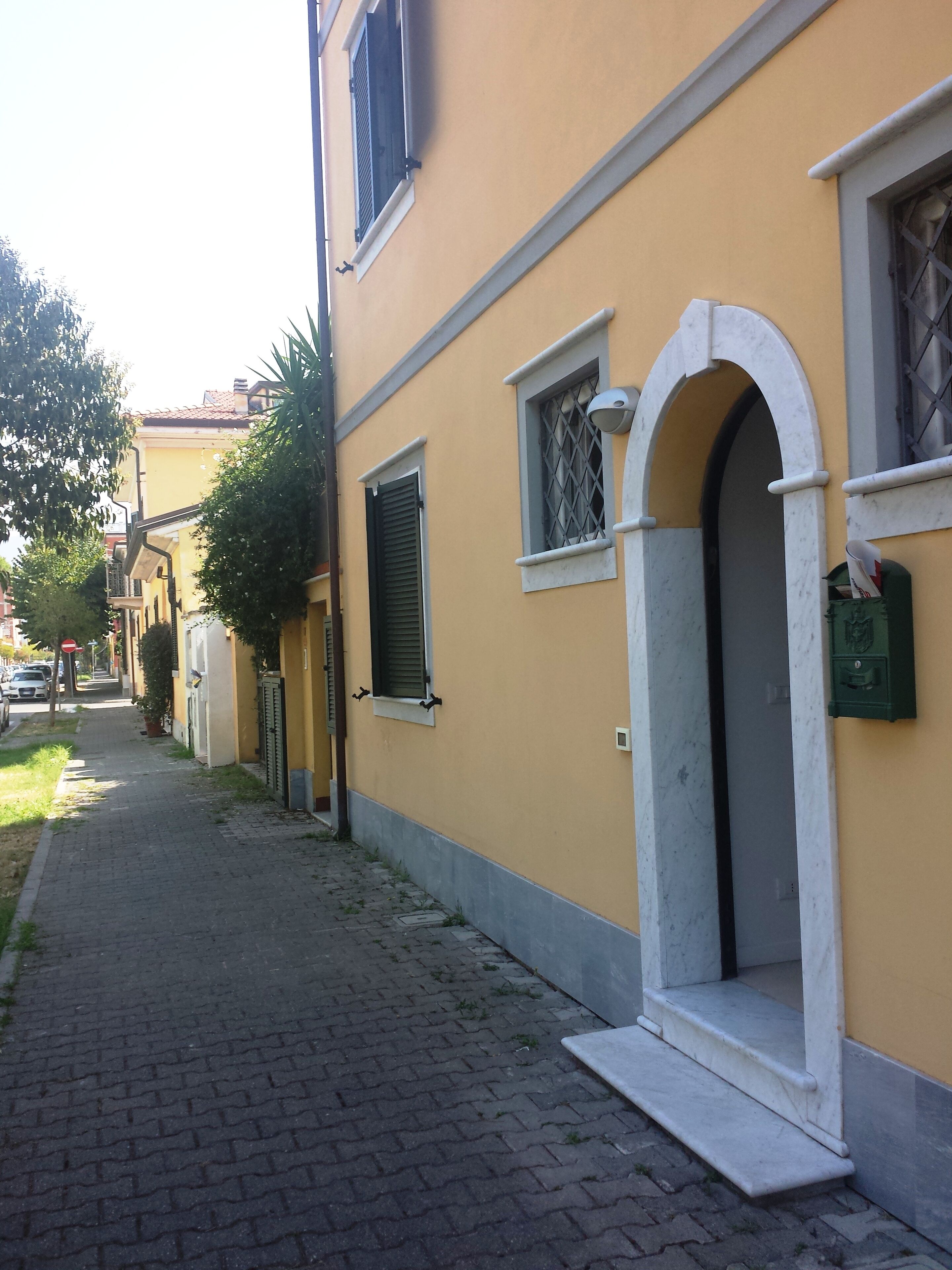 Una estrecha calle empedrada bordeada de edificios amarillos, con una pequeña entrada en arco y un buzón.