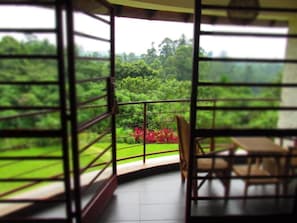 A room with a view of a lush green landscape through large windows. - Koi Koi Cultural Village Hotel (Fort Portal)