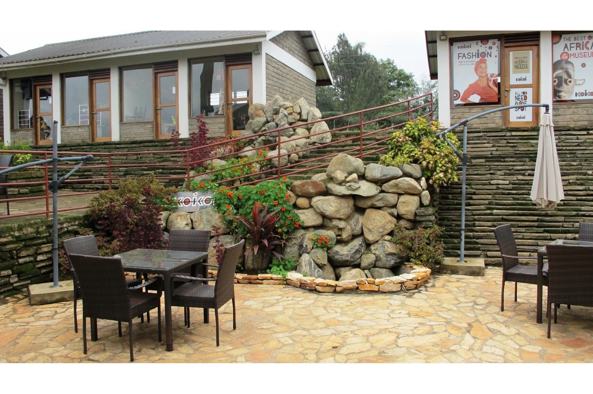 Un patio al aire libre con suelo de piedra, mobiliario de mimbre y una pared de piedra con plantas.