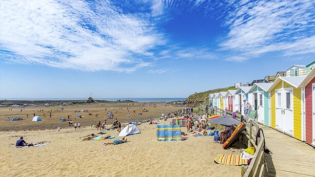Una playa con cabañas de colores, tiendas de campaña y gente relajándose en la arena.