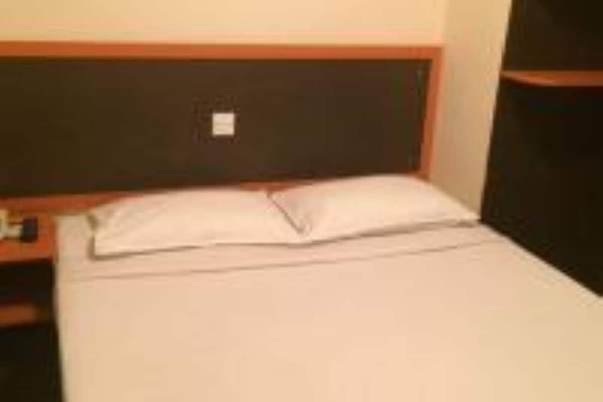 A single bed with a wooden headboard and a white pillow in a hotel room.