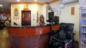 A reception area with a wooden reception desk, a black massage chair, and a refrigerator stocked with beverages. - Kim Tian Hotel Star (Singapore)