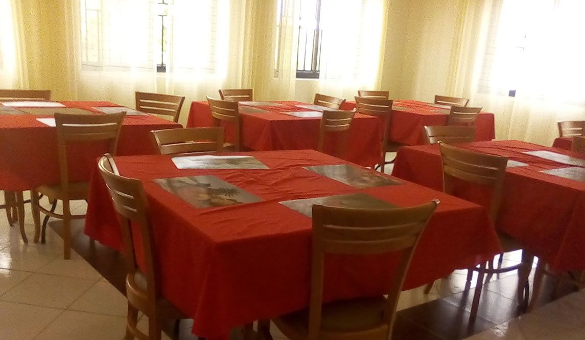 Un espace repas avec plusieurs tables recouvertes de nappes rouges et des chaises en bois.