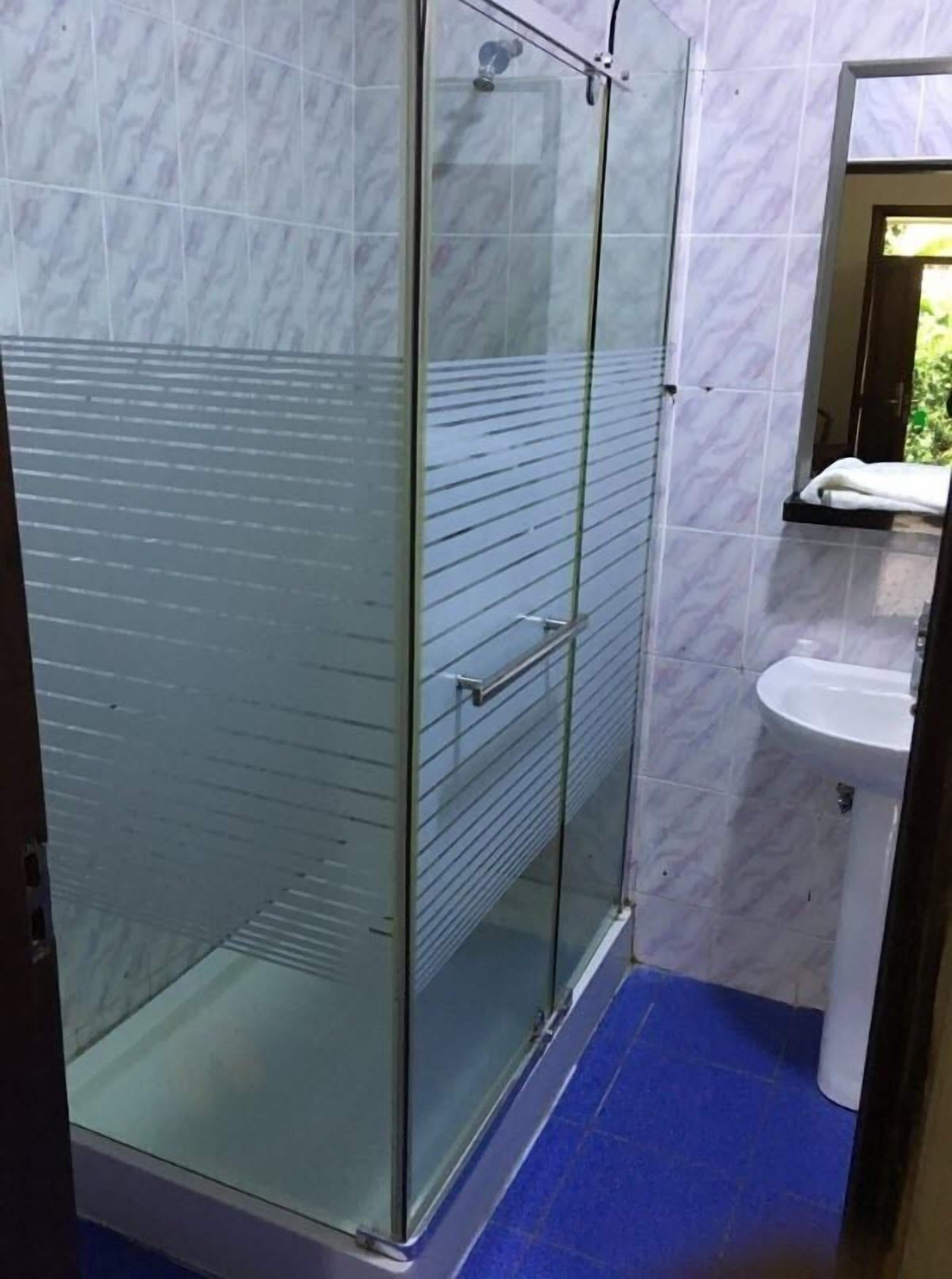 Een badkamer met een douche met glazen wand, een witte wastafel en vloerbedekking van blauwe tegels.