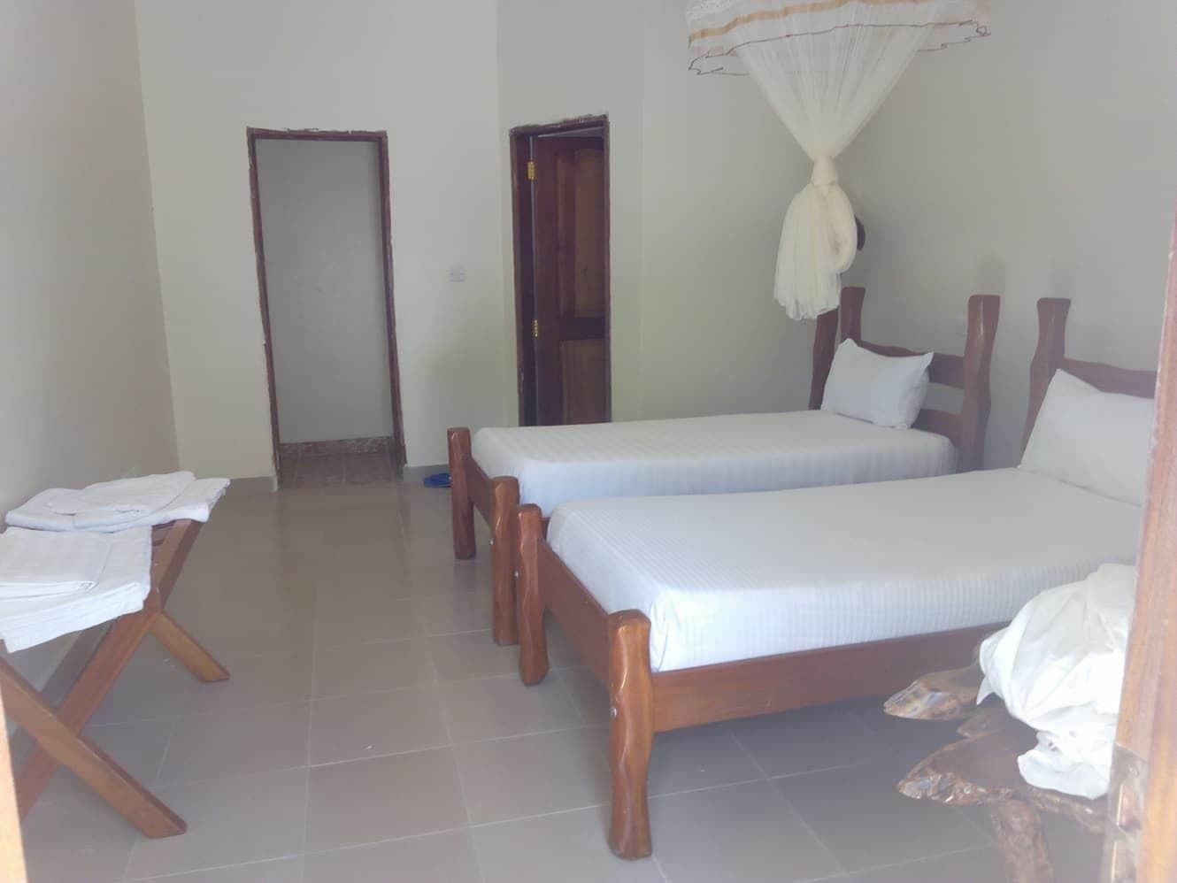 A room with two wooden beds, a bench, and a mosquito net.