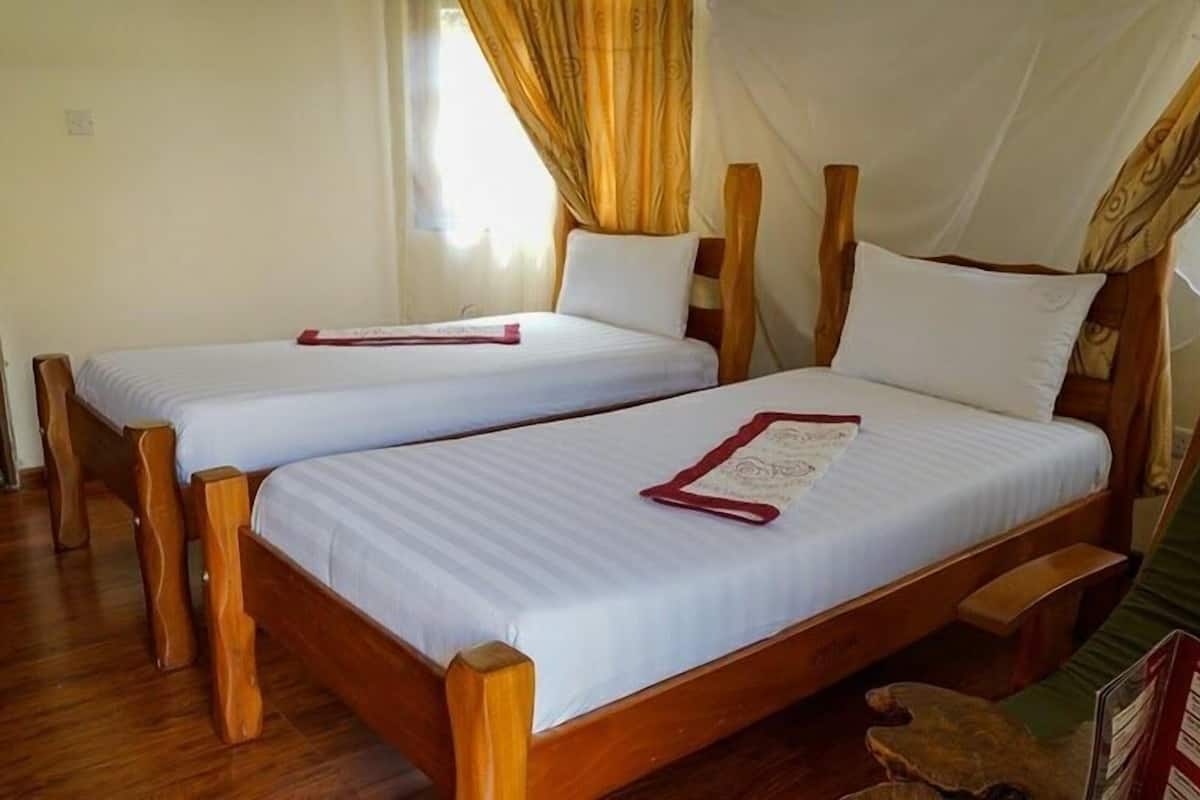 Two wooden beds with white linens and red headboards, a wooden floor, and a window with curtains.