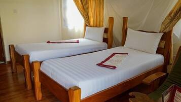 Two wooden beds with white linens and red headboards, a wooden floor, and a window with curtains.