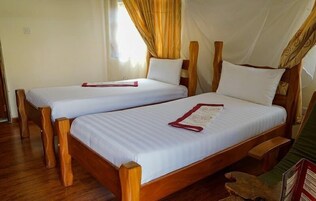 Two wooden beds with white linens and red headboards, a wooden floor, and a window with curtains.