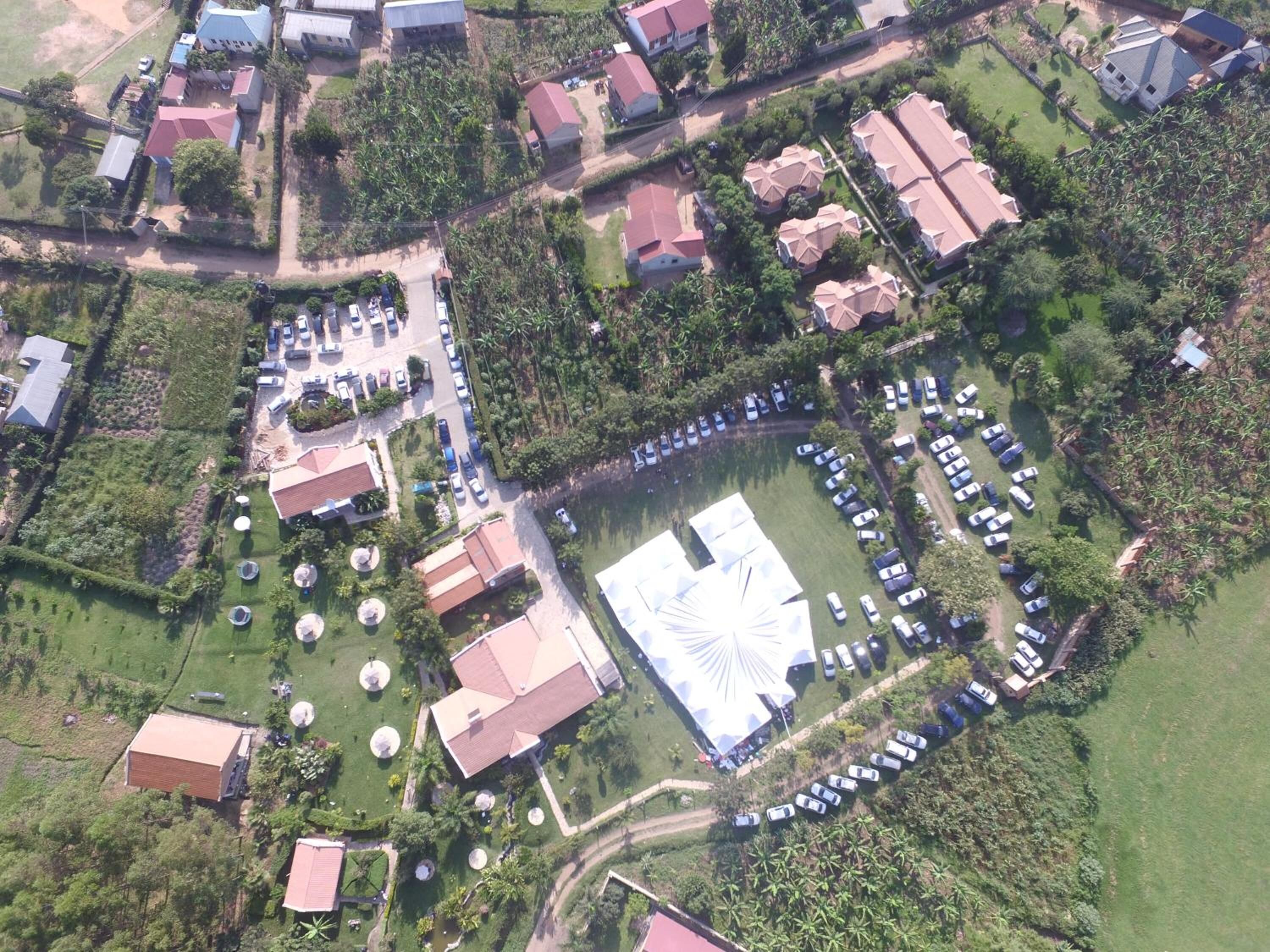 An aerial view of a residential area with multiple houses, a large open space with a white structure, and a parking lot with several cars.