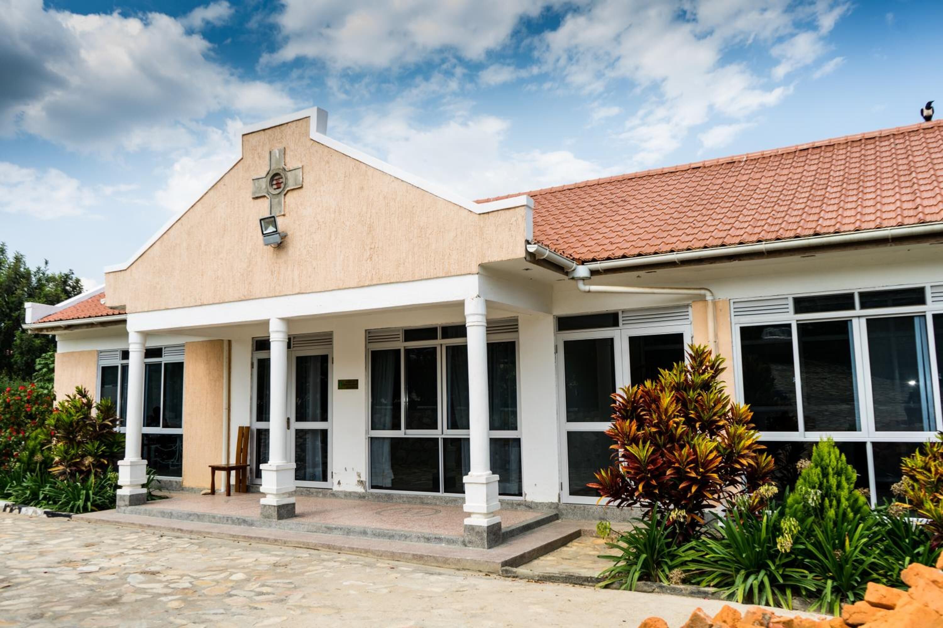 A building with a beige facade, a cross on the front, large windows, and a tiled roof.