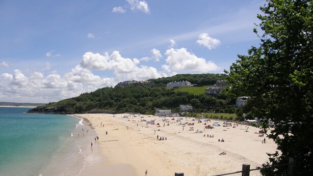 A beach with a wooden fence, a sandy shore, and a backdrop of houses and greenery. - LUXURY APARTMENT PORTH, SLEEPS 4, SEA VIEWS OVERLOOKING WHIPSDERRY BEACH (Porth, Newquay)