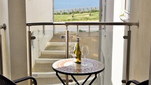 A balcony with a table and chairs, a bottle of wine, and a glass. The balcony overlooks a staircase and a view of the sea. - LUXURY APARTMENT PORTH, SLEEPS 4, SEA VIEWS OVERLOOKING WHIPSDERRY BEACH (Porth, Newquay)