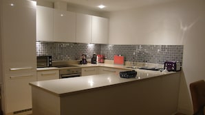 A modern kitchen with white cabinetry, a tiled backsplash, and a central island. - LUXURY APARTMENT PORTH, SLEEPS 4, SEA VIEWS OVERLOOKING WHIPSDERRY BEACH (Porth, Newquay)