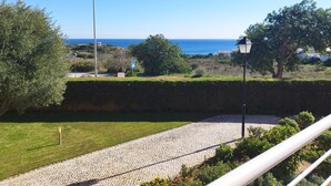 Un camino pavimentado que conduce a una vista panorámica del mar, con un farol y un seto en primer plano.