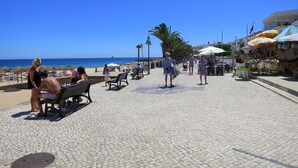 Un paseo marítimo pavimentado con bancos, palmeras y sombrillas de playa.