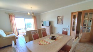 Un comedor con una mesa de madera, sillas acolchadas, un televisor y vistas al exterior.