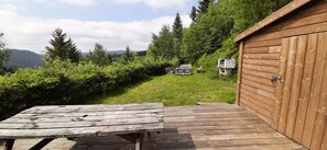 Een houten terras met een picknicktafel, een houten tuinhuis en een gazon met bijenkasten.